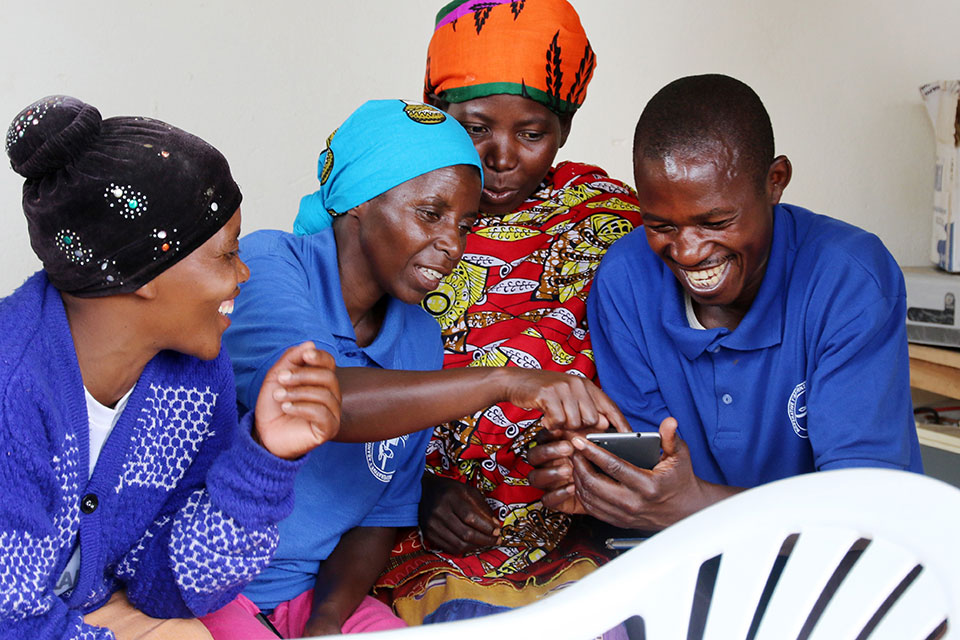 Women and a man in Rwanda check the "Buy From Women" mobile platform on a cell phone. Photo: UN Women/Sandra Hollinger