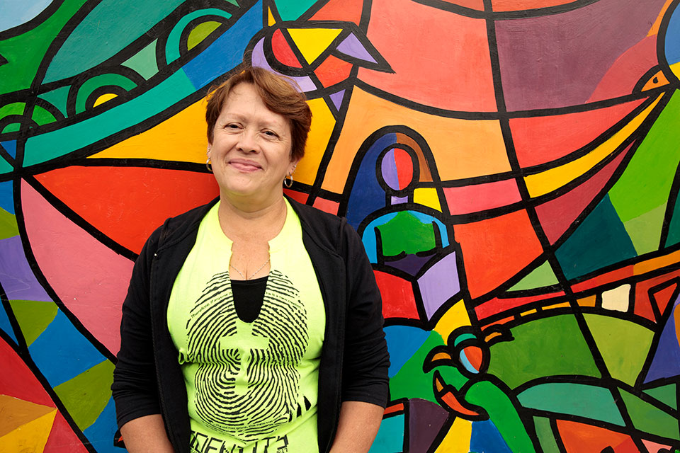 Alba Morena Fernandez, 56, resident of Zone 5, Guatemala City, poses in front of the mural residents painted as part of a larger initiative to engage women and their community in reclaiming streets, parks and public spaces, as part of the Safe City programme. Photo: UN Women/Ryan Brown